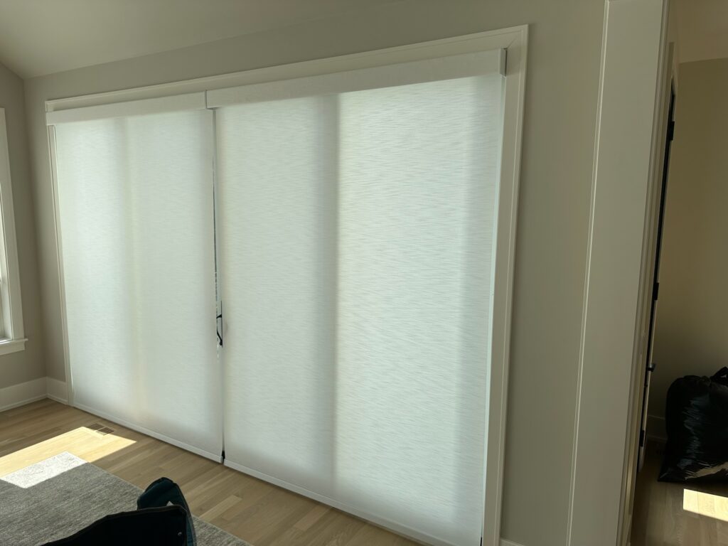 Two hunter Douglas alustra woven textures roller shades over a back sliding door.