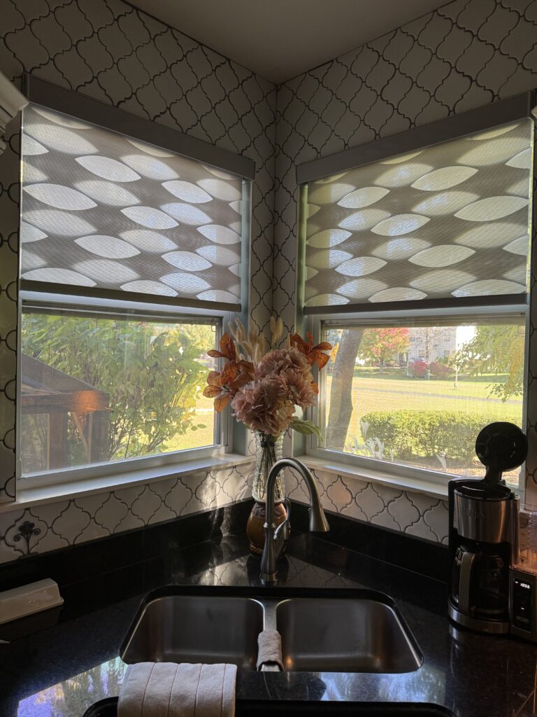 Circular patterned Hunter Douglas Banded Shades hanging above a sink window, surrounded by white backsplash